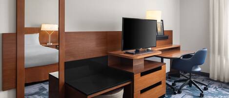 A hotel room with a bed, a desk with a computer, a chair, a television, and a mirror.