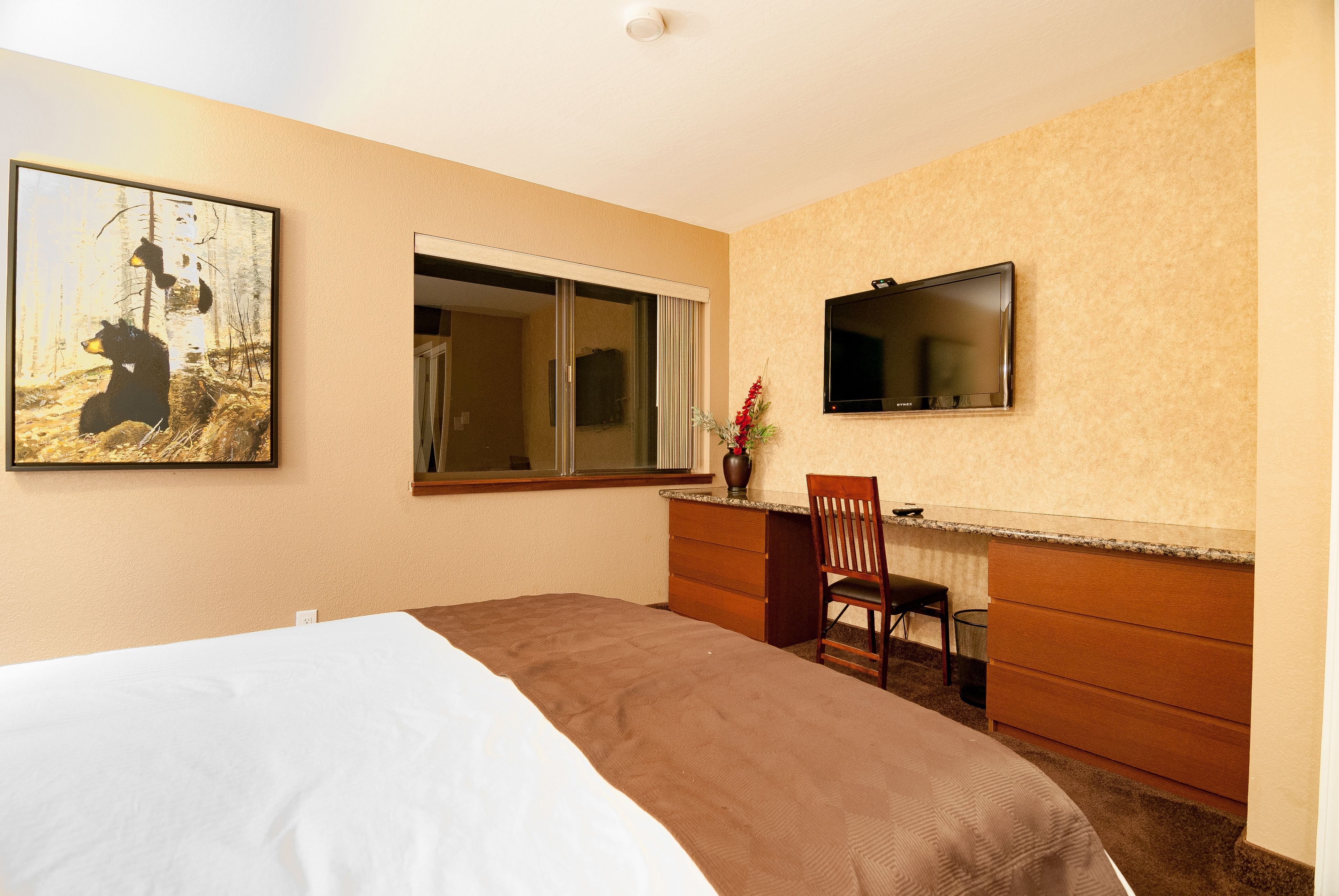 A hotel room with a bed, a desk with a chair, a TV, and a painting on the wall.