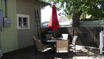 A patio with a table and chairs, a red umbrella, and a wooden fence.
