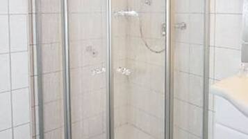 A glass-enclosed shower stall with a white tiled floor and a white sink to the right.