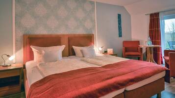 Ein Doppelbett mit Holz Kopfteil, eine rote Tagesdecke, zwei Nachttische mit Lampen, ein roter Sessel und ein kleiner Tisch mit Flasche und Gläsern.