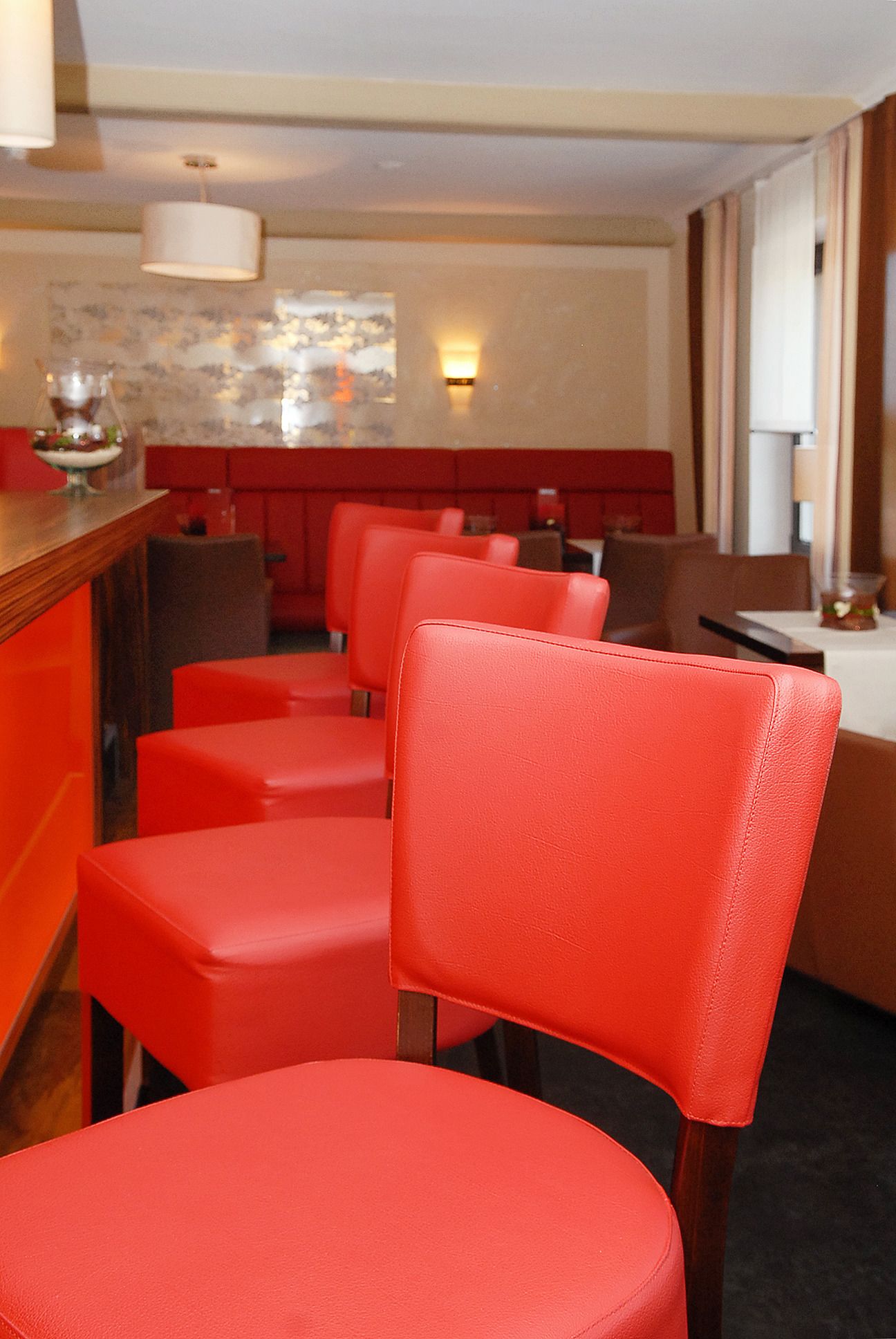 A row of red upholstered chairs and a wooden bar counter in a restaurant setting.