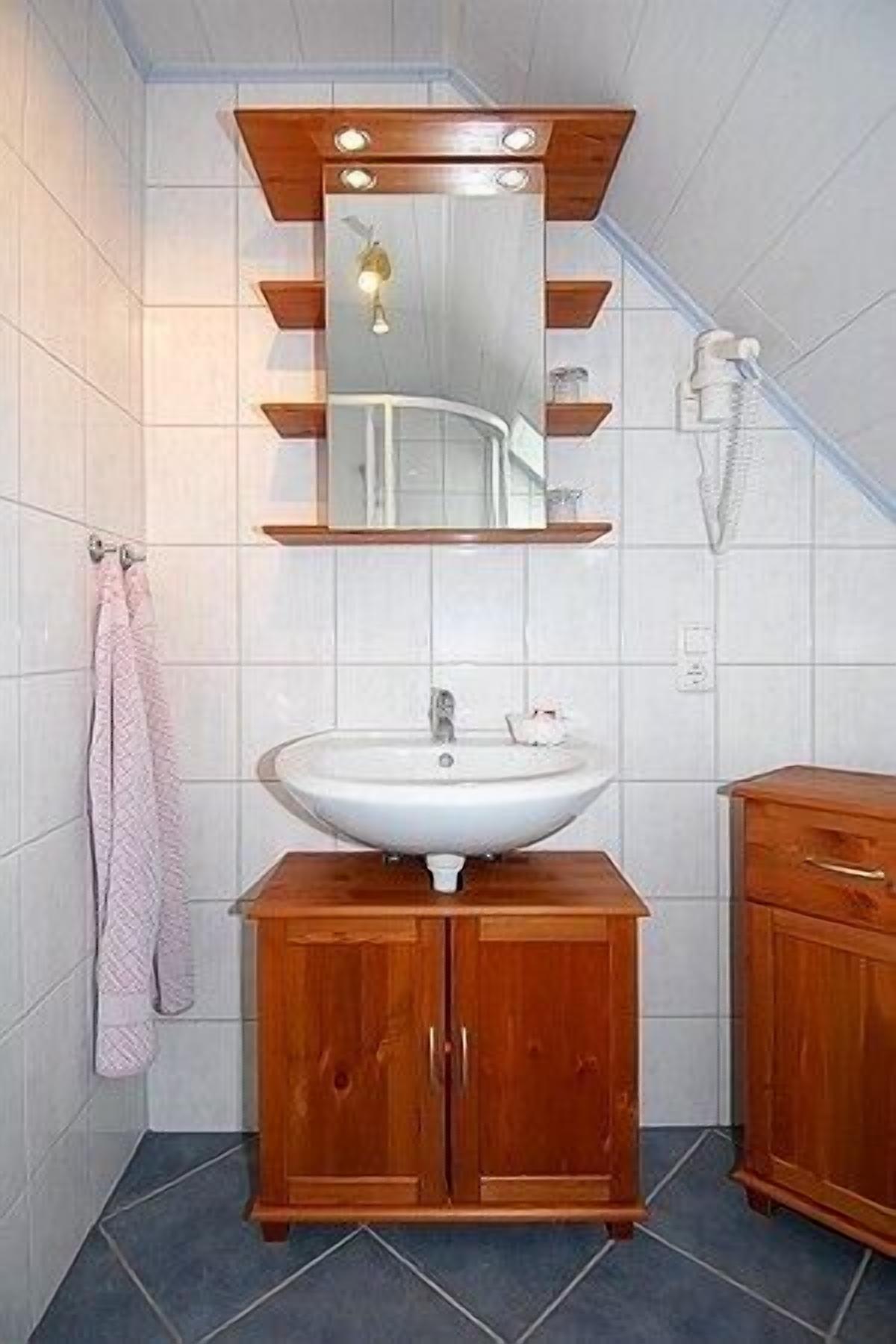 Een badkamer met een witte wastafel, houten kastjes, een spiegel en een handdoekrek.