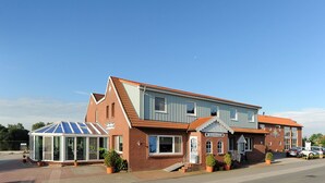 A two-story building with a glass conservatory, a brick facade, and a red-tiled roof. - Hotel & Restaurant Nordstern (Neuharlingersiel)