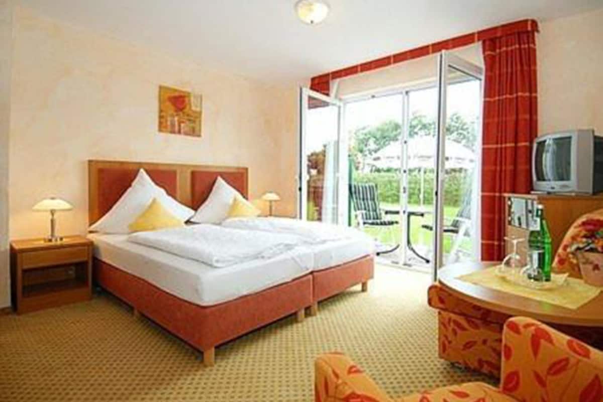 Habitación de hotel con cama doble, una mesita con televisor y vistas al exterior a través de una puerta corrediza de vidrio.