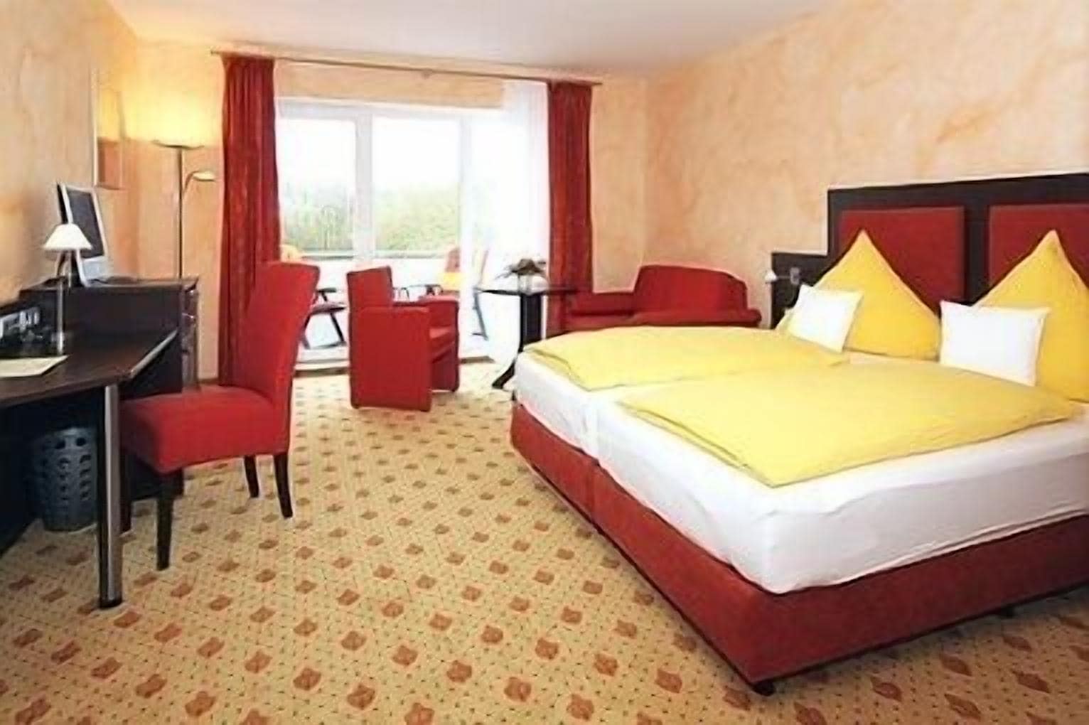 Ein Hotelzimmer mit einem Bett, zwei roten Sesseln, einem Schreibtisch und einer Lampe.