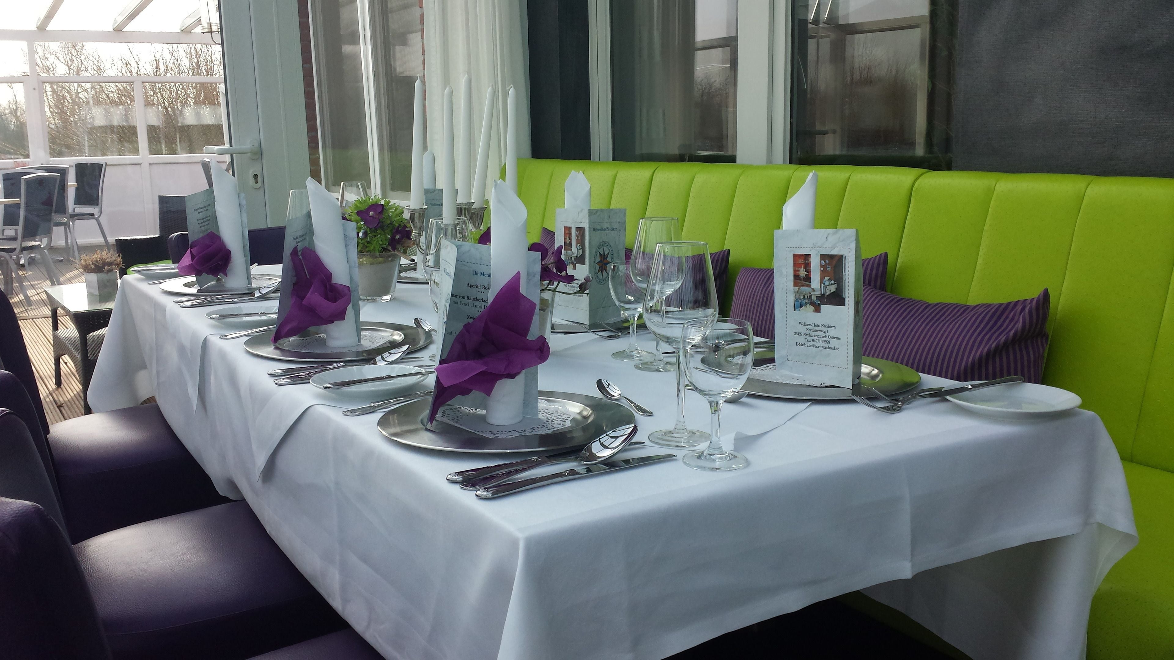 Un restaurant avec des tables dressées pour le service, nappes blanches et serviettes violettes.