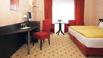 Een hotelkamer met een bed, een bureau, een stoel, een tafeltje en een raam met gordijnen.