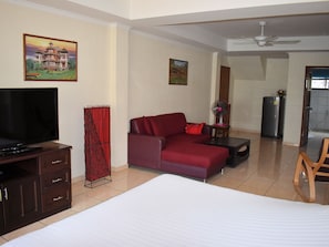 A hotel room with a bed, a red sofa, a TV, a fan, and a refrigerator. - Klein Heidelberg (Pattaya)