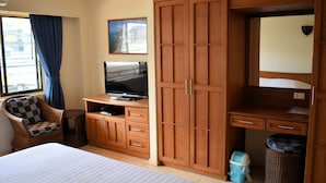 A hotel room with a bed, a television on a wooden cabinet, a wardrobe, a chair, and a window with curtains. - Klein Heidelberg (Pattaya)