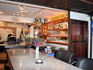 A bar area with a counter, bar stools, and shelves stocked with bottles and glasses. - Klein Heidelberg (Pattaya)