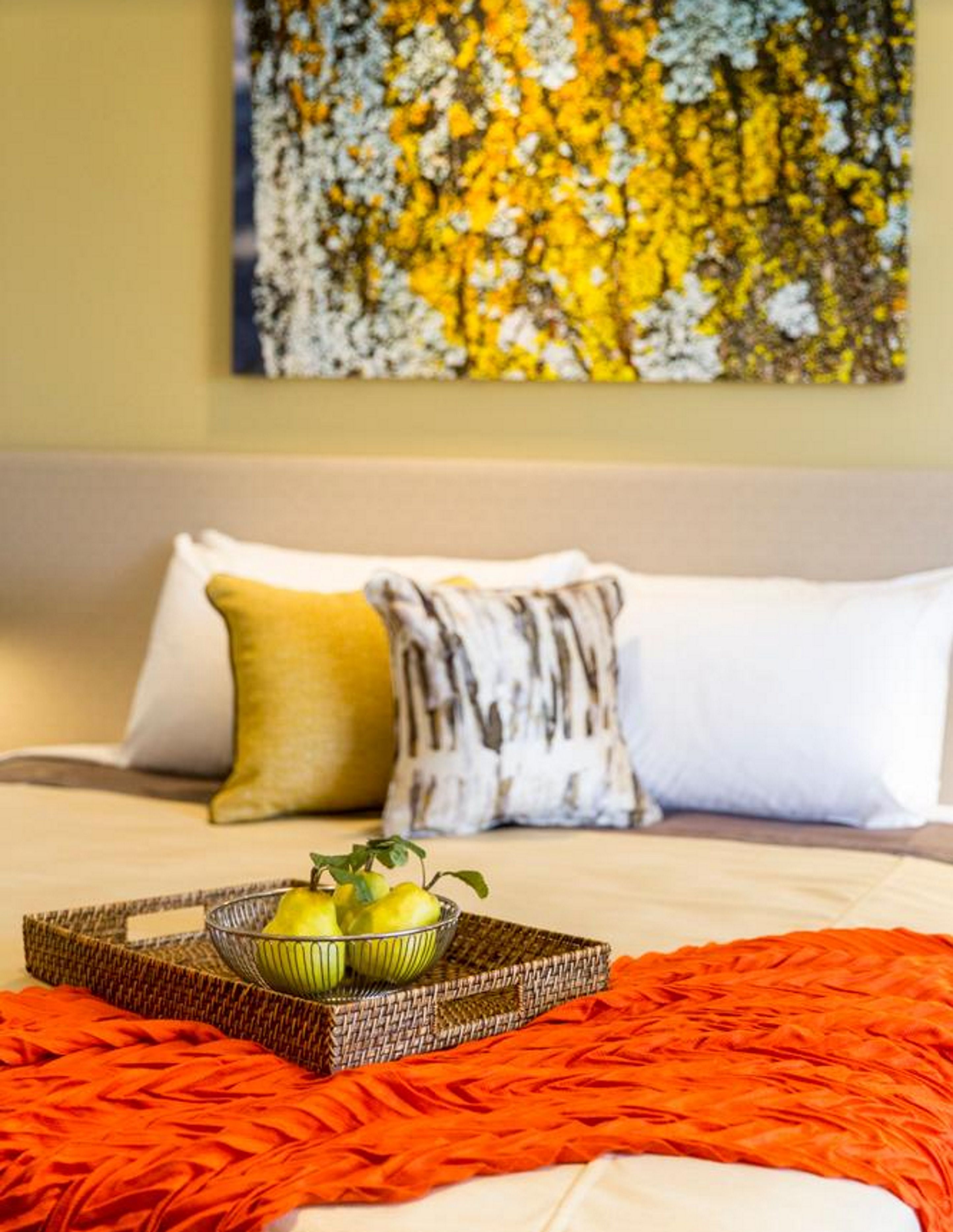 A hotel room with a bed, a tray with fruits, and a painting on the wall.