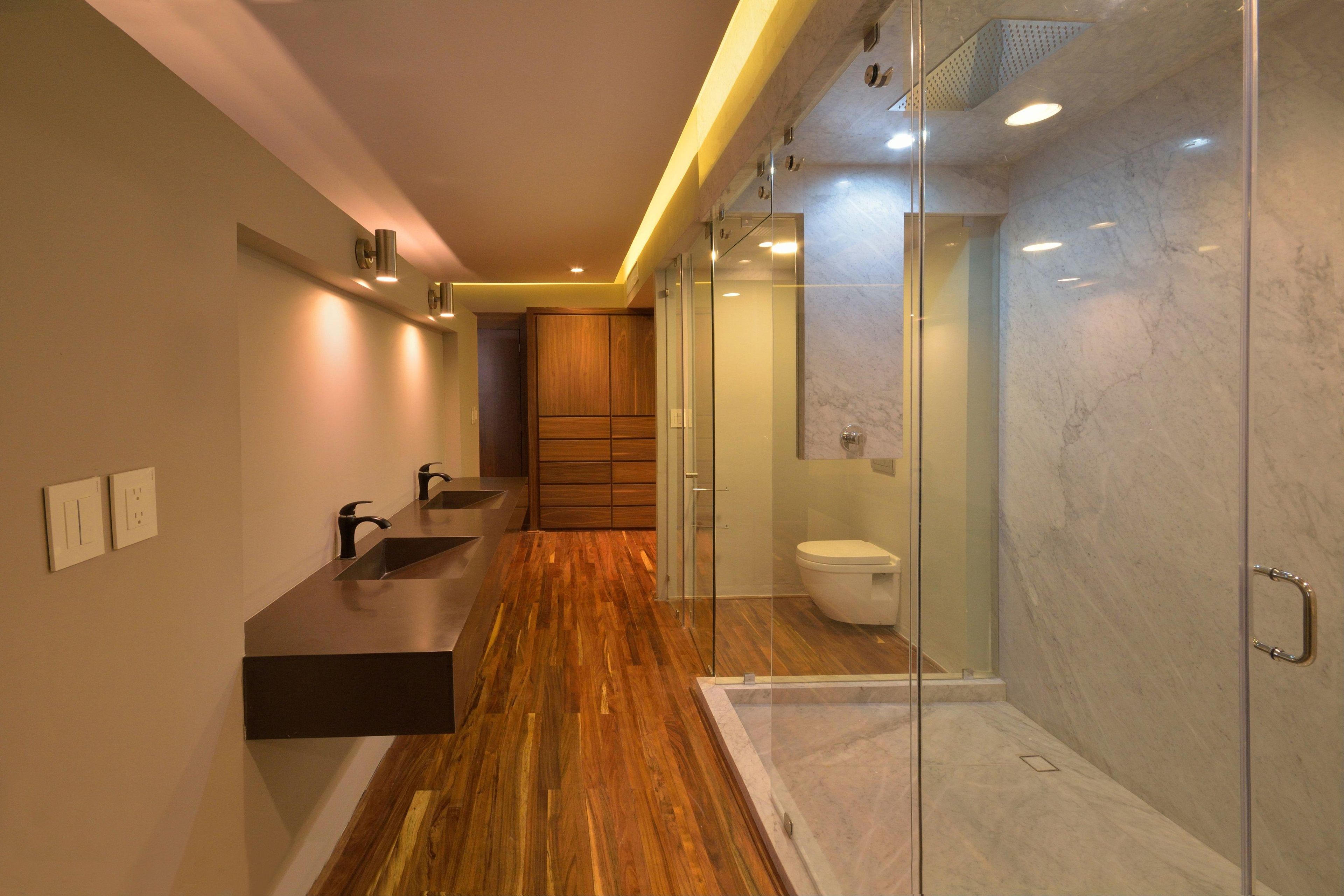 A modern bathroom with a wooden vanity, a glass shower enclosure, and a marble-tiled wall.