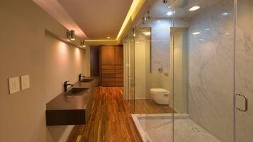 A modern bathroom with a wooden vanity, a glass shower enclosure, and a marble-tiled wall.