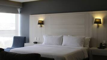 A hotel room with a large bed, two bedside lamps, a chair, and a nightstand with a phone.