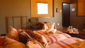 A hotel room with a bed, a chair, a table with a pitcher and glasses, and a window with blinds.