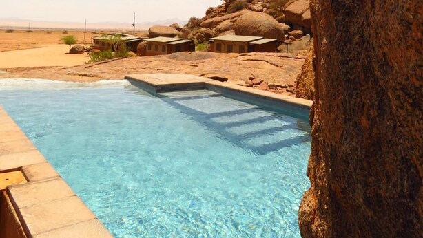 A clear blue pool with a rocky landscape and a large rock in the foreground.