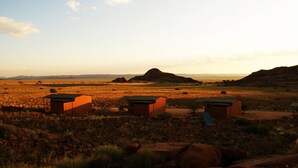 A desert landscape with three small, rectangular buildings with flat roofs, likely used for accommodation or storage.