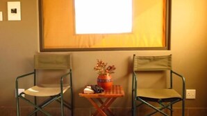 Two green metal chairs with cushions, a small wooden table with a vase of flowers, and a window with a white blind.