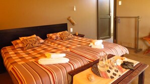 A hotel room with a large bed, a bedside table with a bottle, glasses, and a remote control.