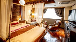 Une chambre d’hôtel avec un grand lit, un coin salon avec un fauteuil, une télévision et un minibar.