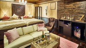 Une chambre d’hôtel comprenant un lit, un canapé, un fauteuil, une table basse avec des bouteilles et un minibar.