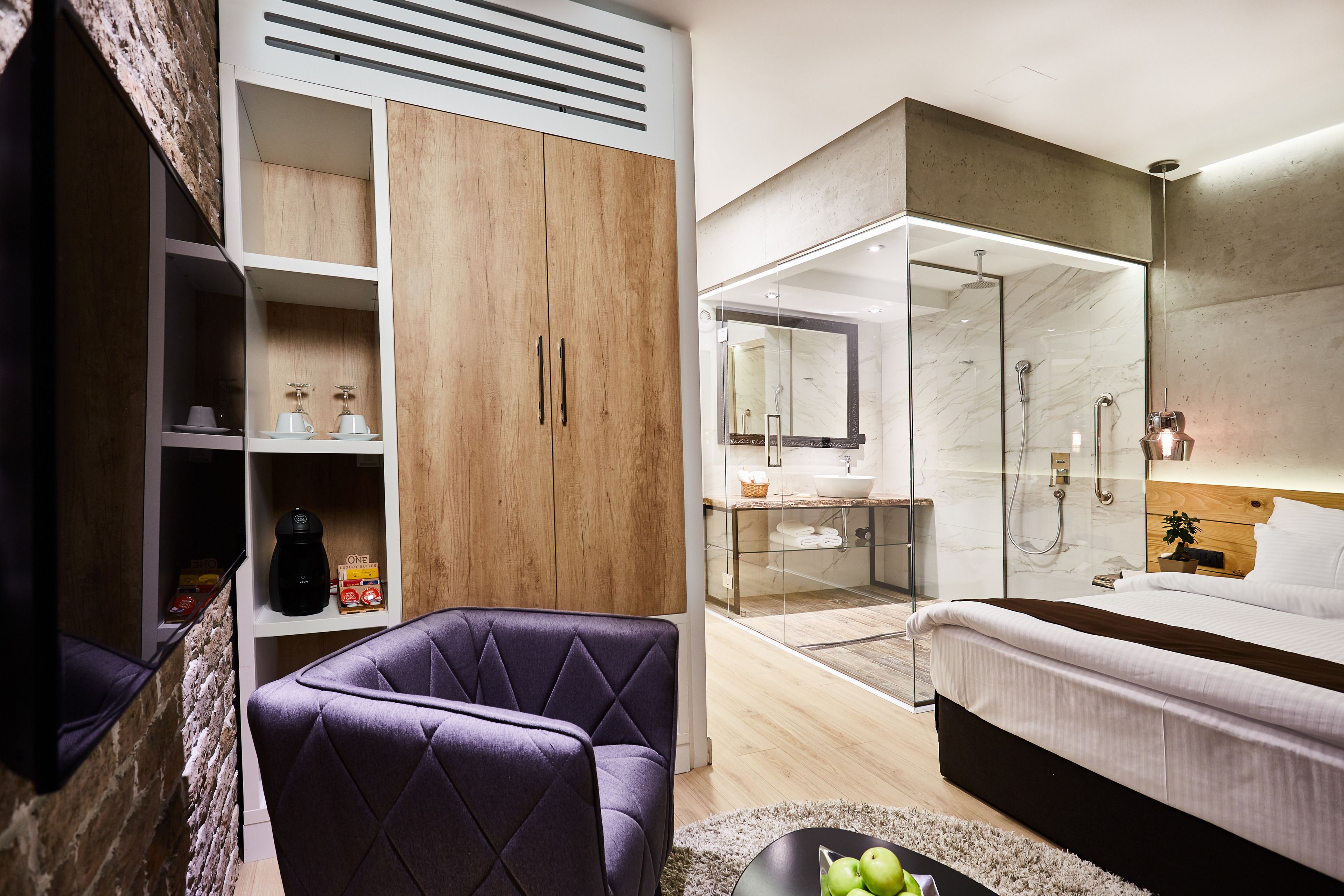 Un dormitorio moderno con una cama grande, una zona de estar, un baño con ducha de vidrio y un armario de madera.