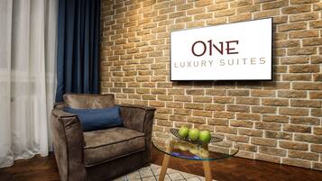 Un salón moderno con una pared de ladrillo, un sofá de cuero marrón, una mesa de centro de vidrio con manzanas y un letrero que dice "ONE LUXURY SUITES".