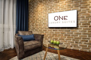 Un salón moderno con una pared de ladrillo, un sofá de cuero marrón, una mesa de centro de vidrio con manzanas y un letrero que dice "ONE LUXURY SUITES".