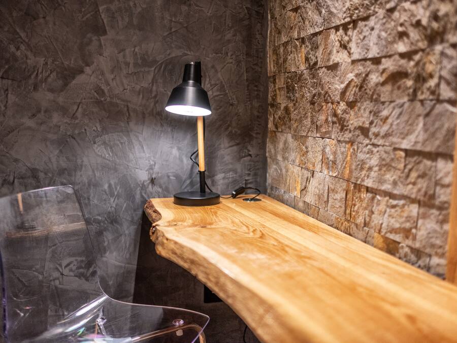 Een houten bank met een transparante glazen stoel, een zwarte bureaulamp en een stenen muur.