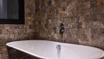 Un baño moderno con una bañera independiente, azulejos de piedra y un espejo con marco negro.