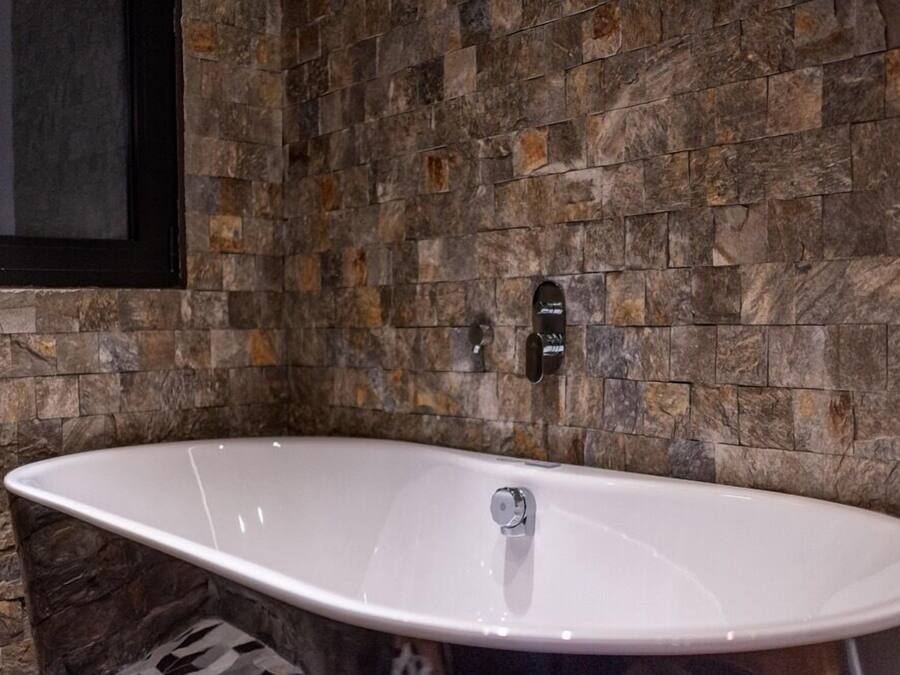 Un baño moderno con una bañera independiente, azulejos de piedra y un espejo con marco negro.