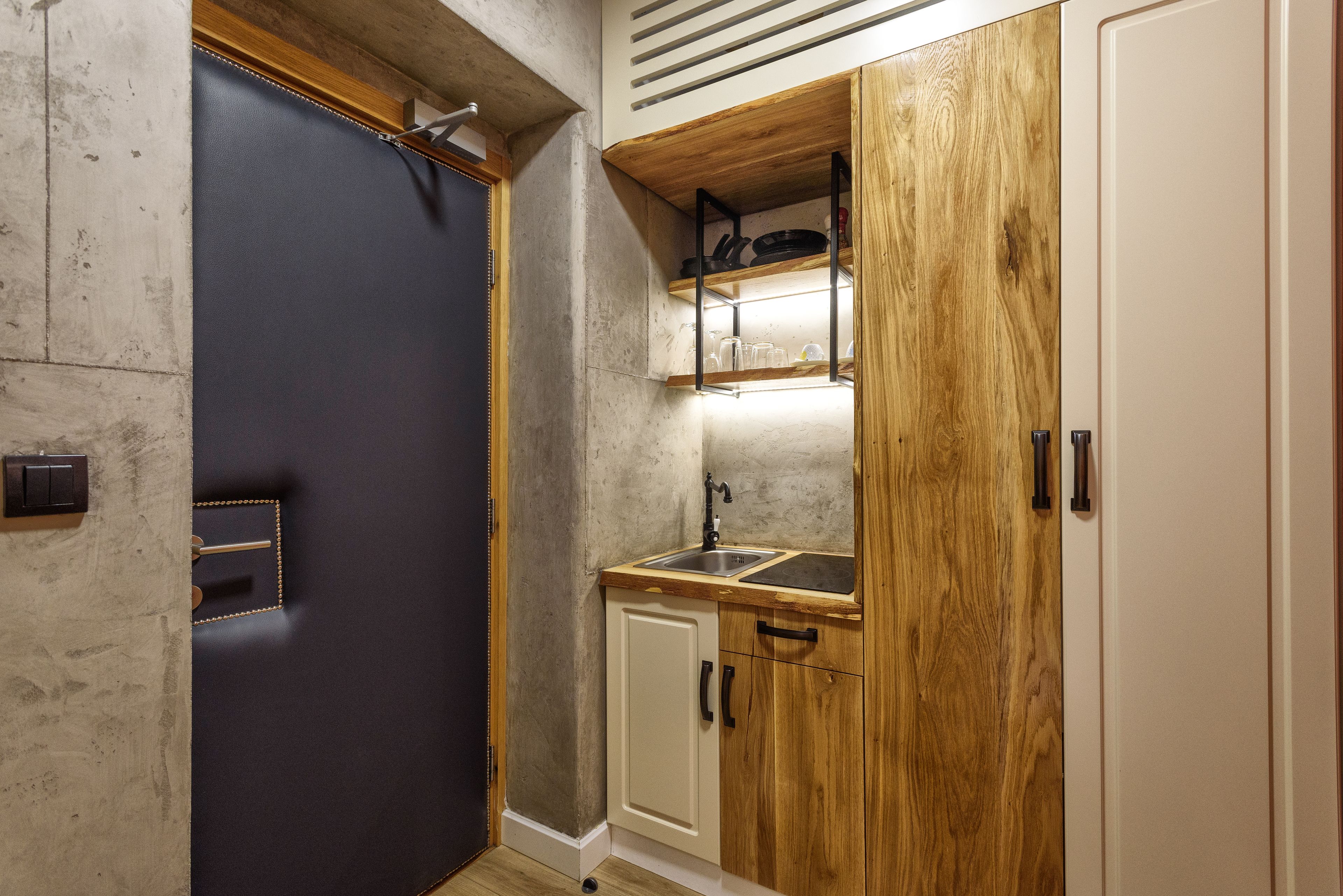 Une cuisine de taille réduite, dotée d’une porte sombre, de meubles en bois et d’un petit plan de travail avec un évier.