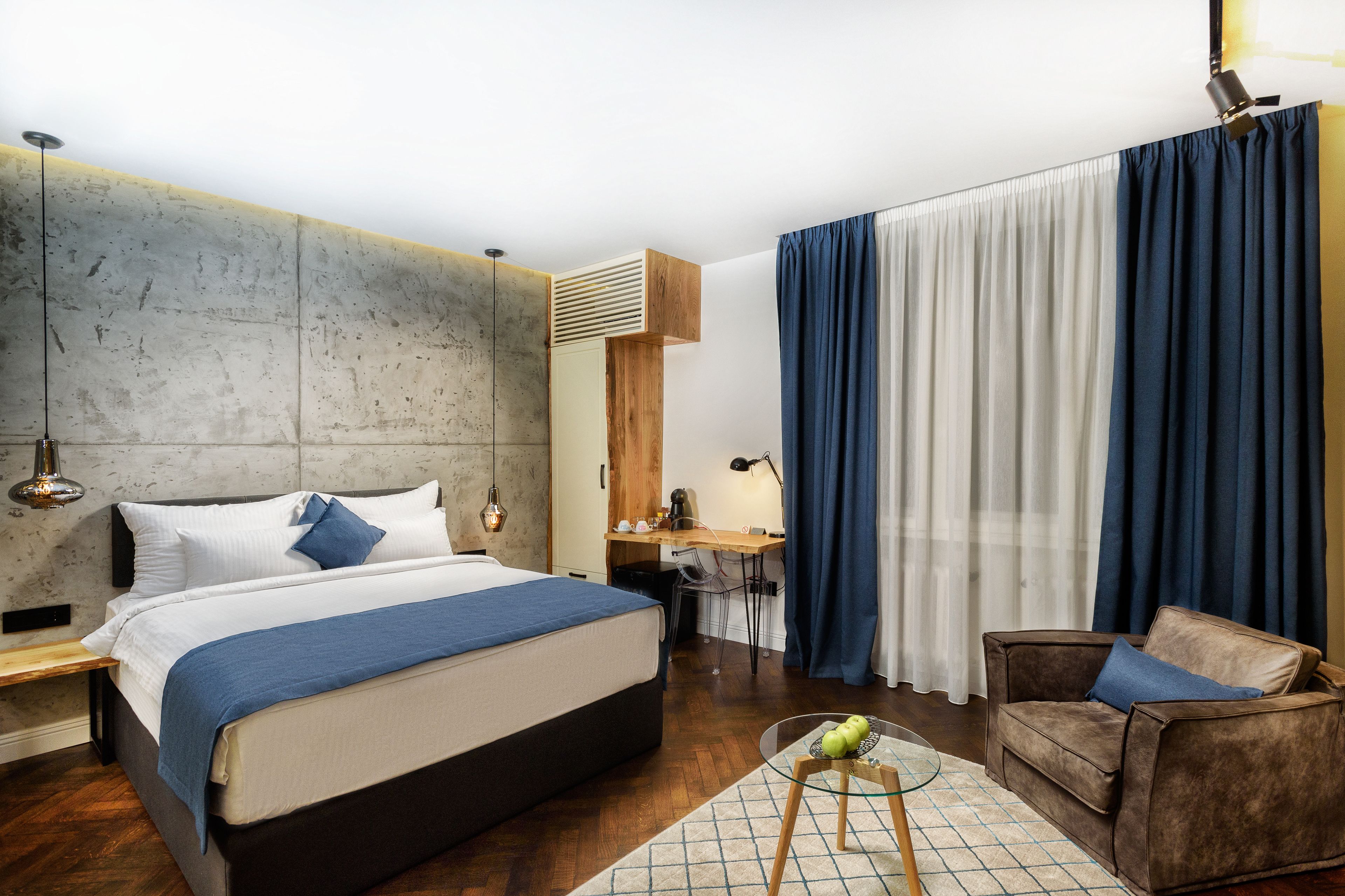 Habitación de hotel moderna con una cama grande, un escritorio, un sofá y una mesa de vidrio con manzanas.