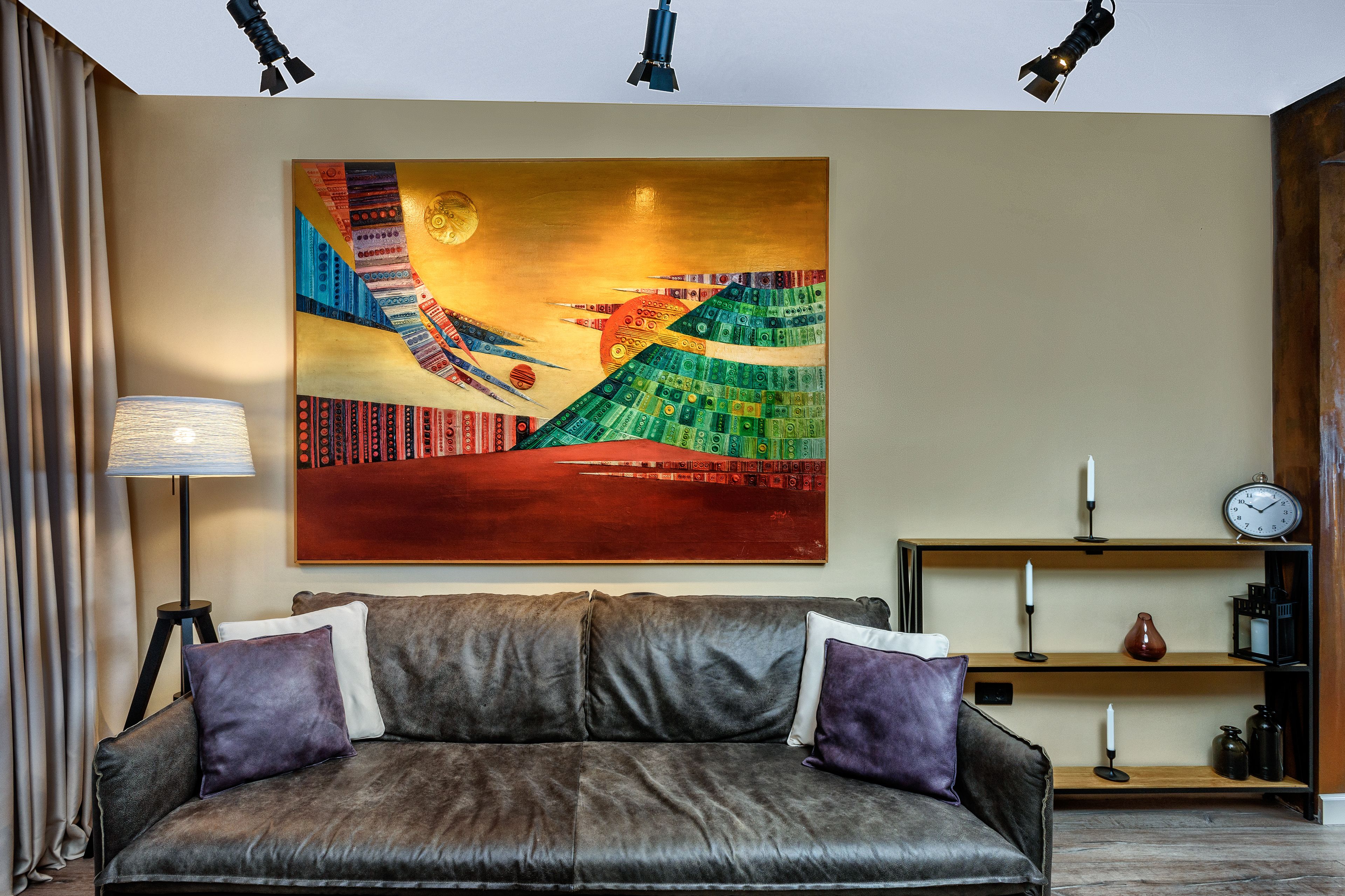 A modern living room with a large abstract painting, a leather sofa, a lamp, and a shelf with decorative items.