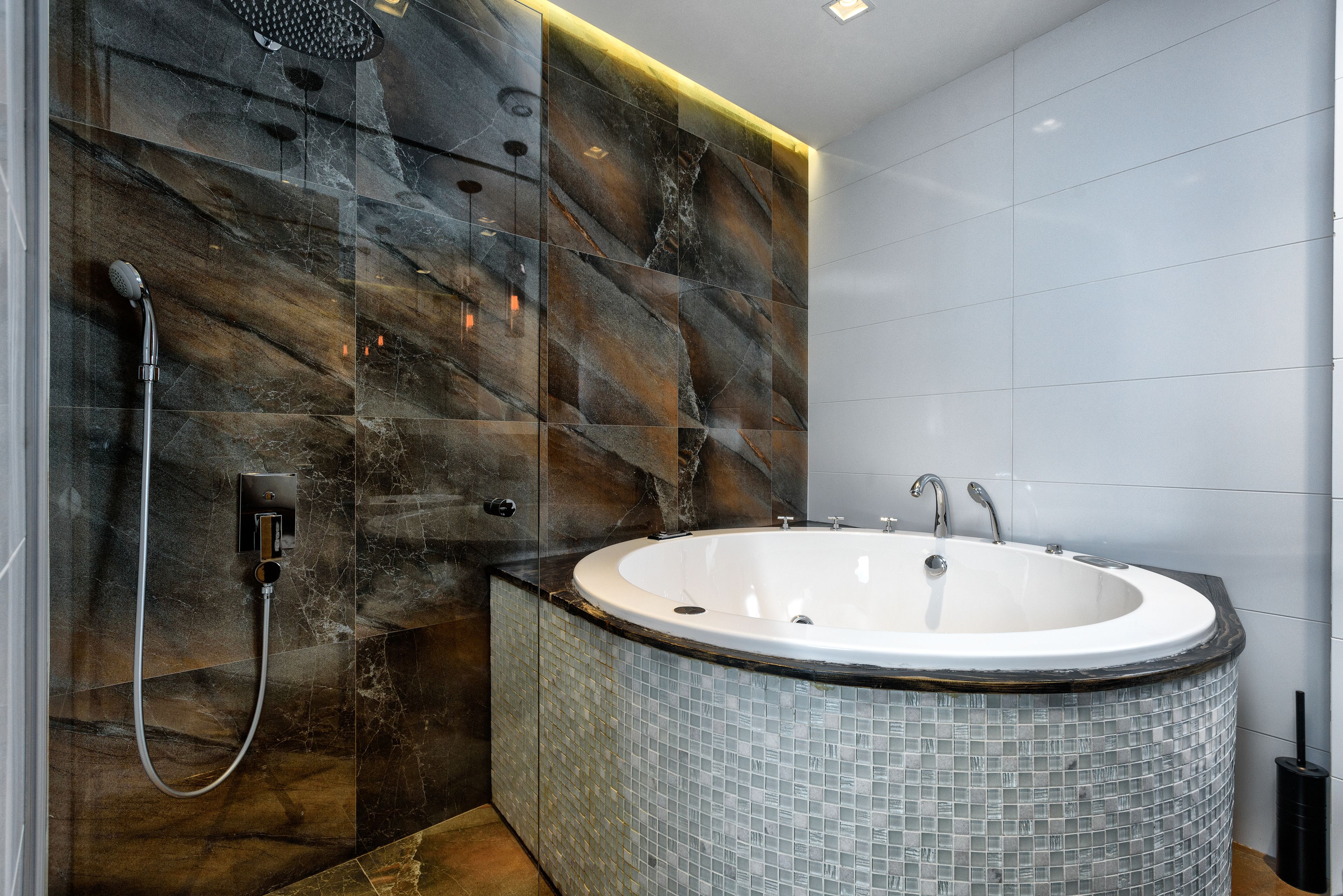 A modern bathroom with a freestanding bathtub, a showerhead, and a tiled wall.