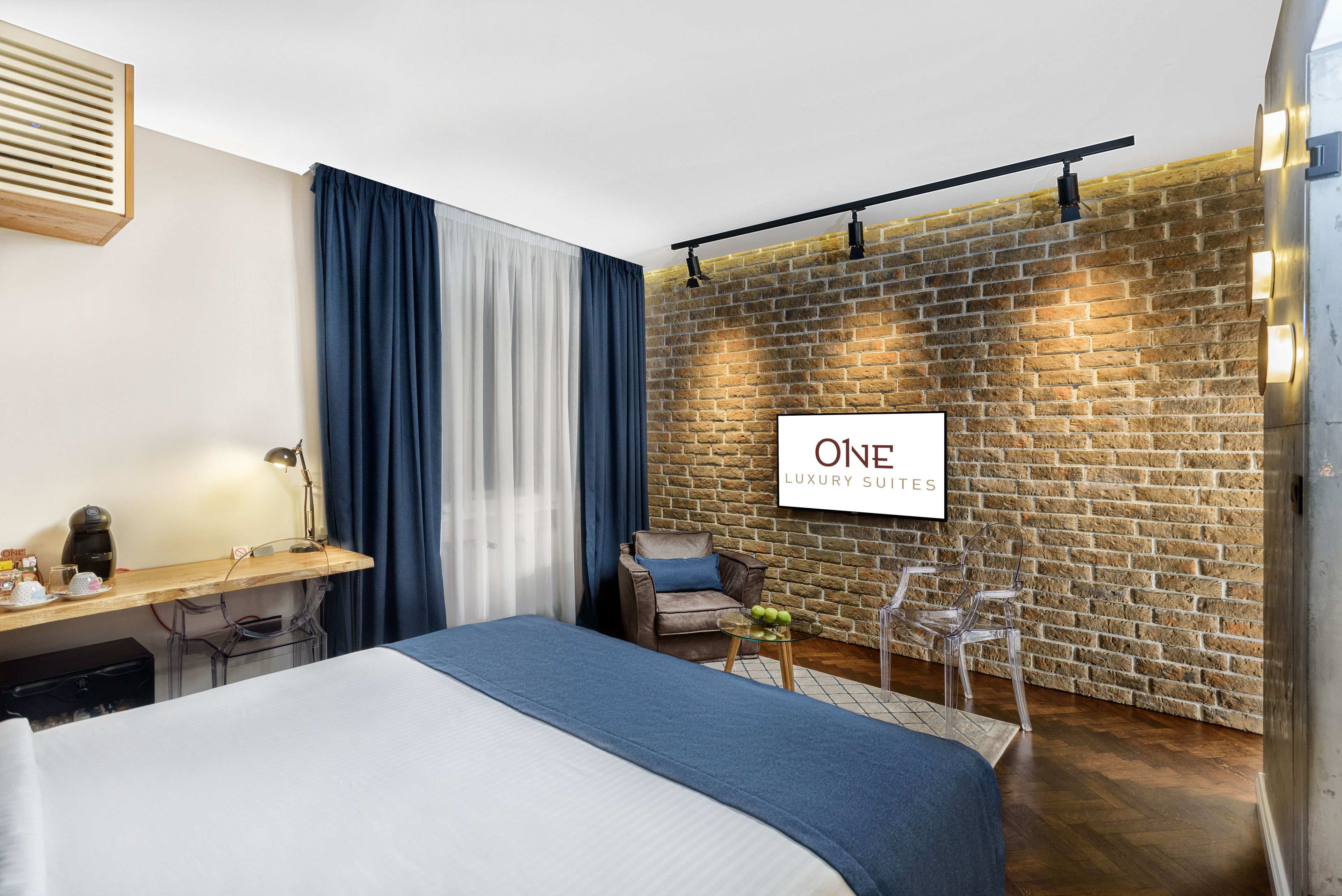 A modern hotel room with a brick wall, a bed, a desk, and a chair.