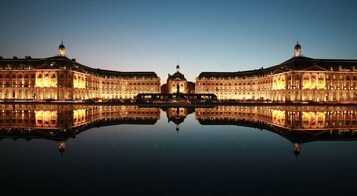 Un edificio simétrico con un patio central y una estatua, reflejado en aguas tranquilas.