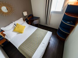 Una habitación de hotel con cama, escritorio, silla, espejo y ventana con cortinas.