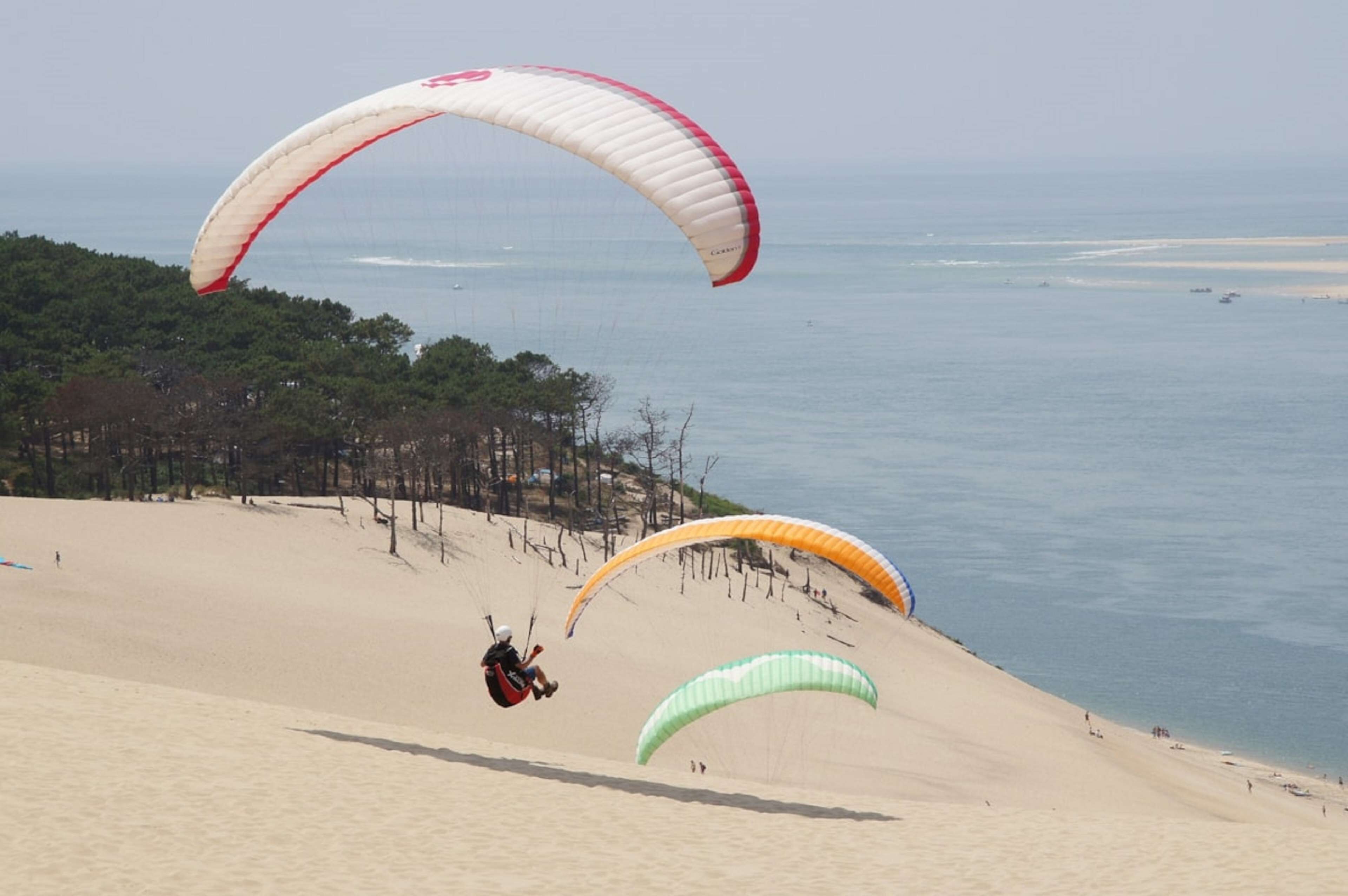 A sandy beach with three parachutes descending.