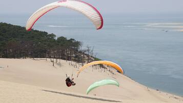 A sandy beach with three parachutes descending.