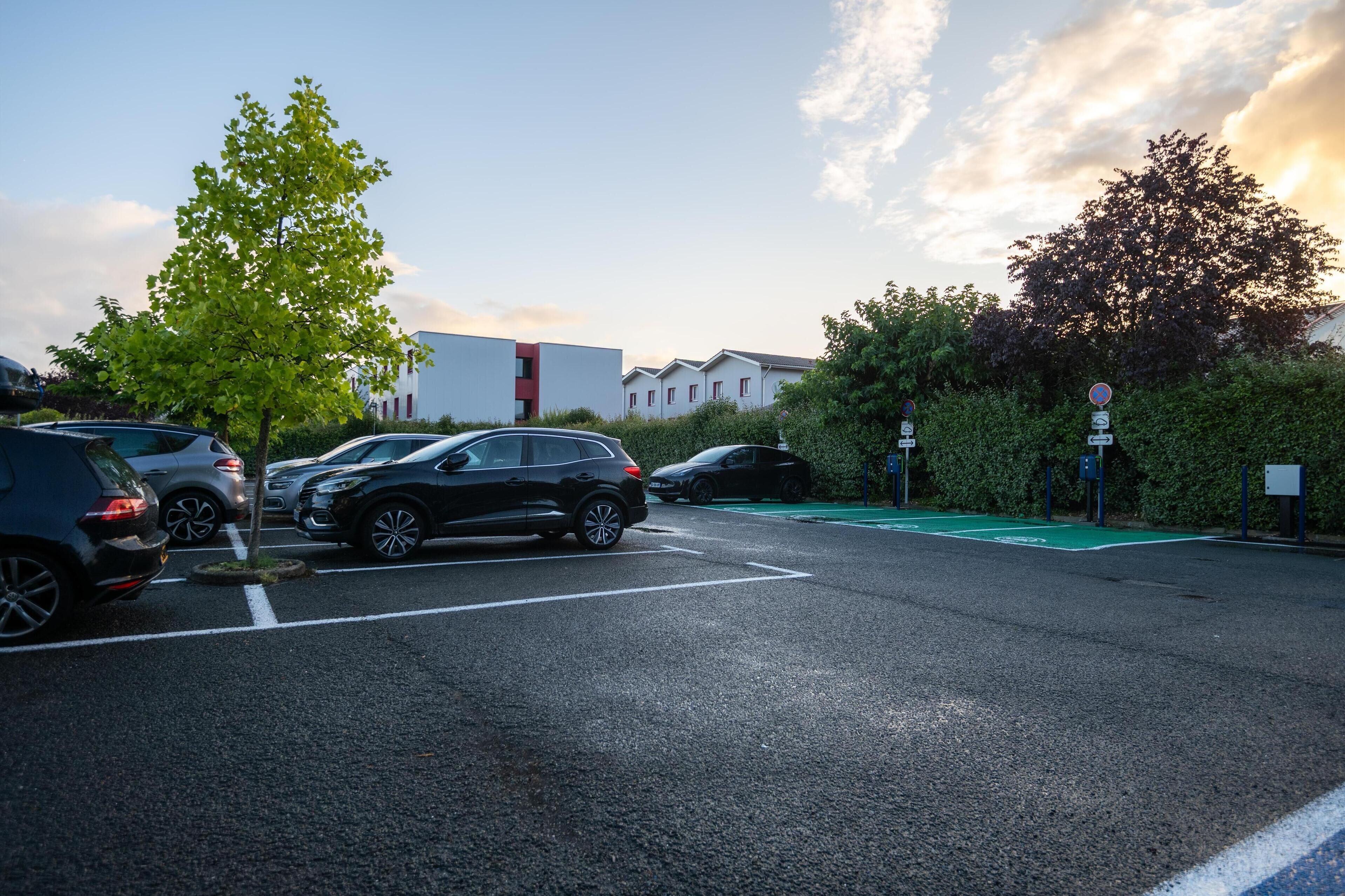 Un estacionamiento con varios coches, un carril bici verde y edificios al fondo.