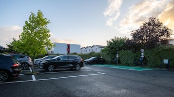 Un estacionamiento con varios coches, un carril bici verde y edificios al fondo.