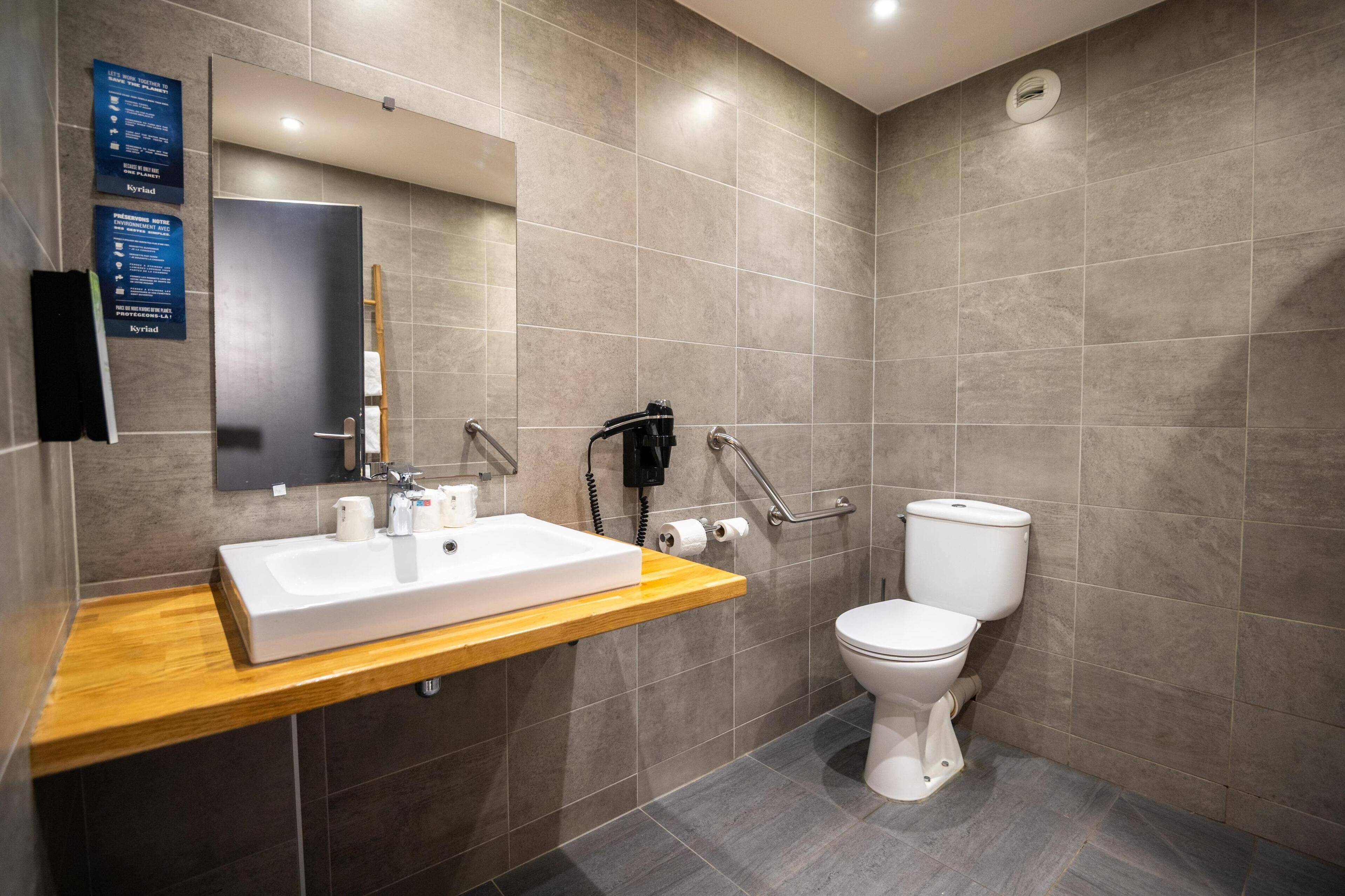 Une salle de bain moderne avec un meuble-lavabo en bois, un lavabo blanc, des toilettes et un sèche-mains.