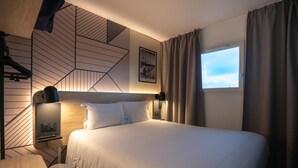 A hotel room with a large bed, a desk, a chair, a wall-mounted TV, and a window with curtains. - KYRIAD BORDEAUX SUD - Villenave d'Ornon (Villenave-d'Ornon)