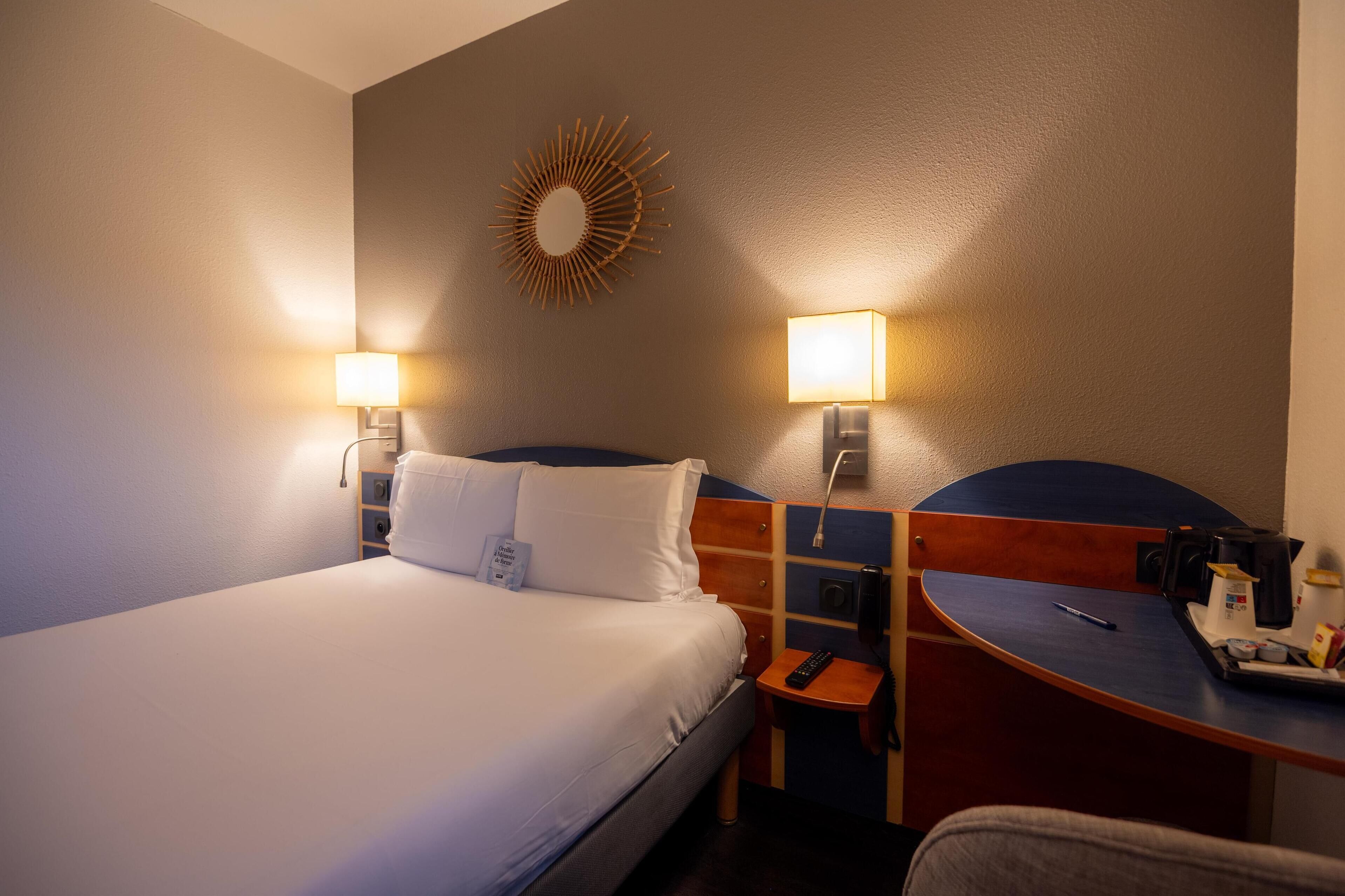 A hotel room with a bed, bedside lamps, a desk with a chair, and a wall-mounted mirror.