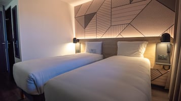 A hotel room with two beds, a geometric patterned wall, bedside lamps, and a wooden headboard.