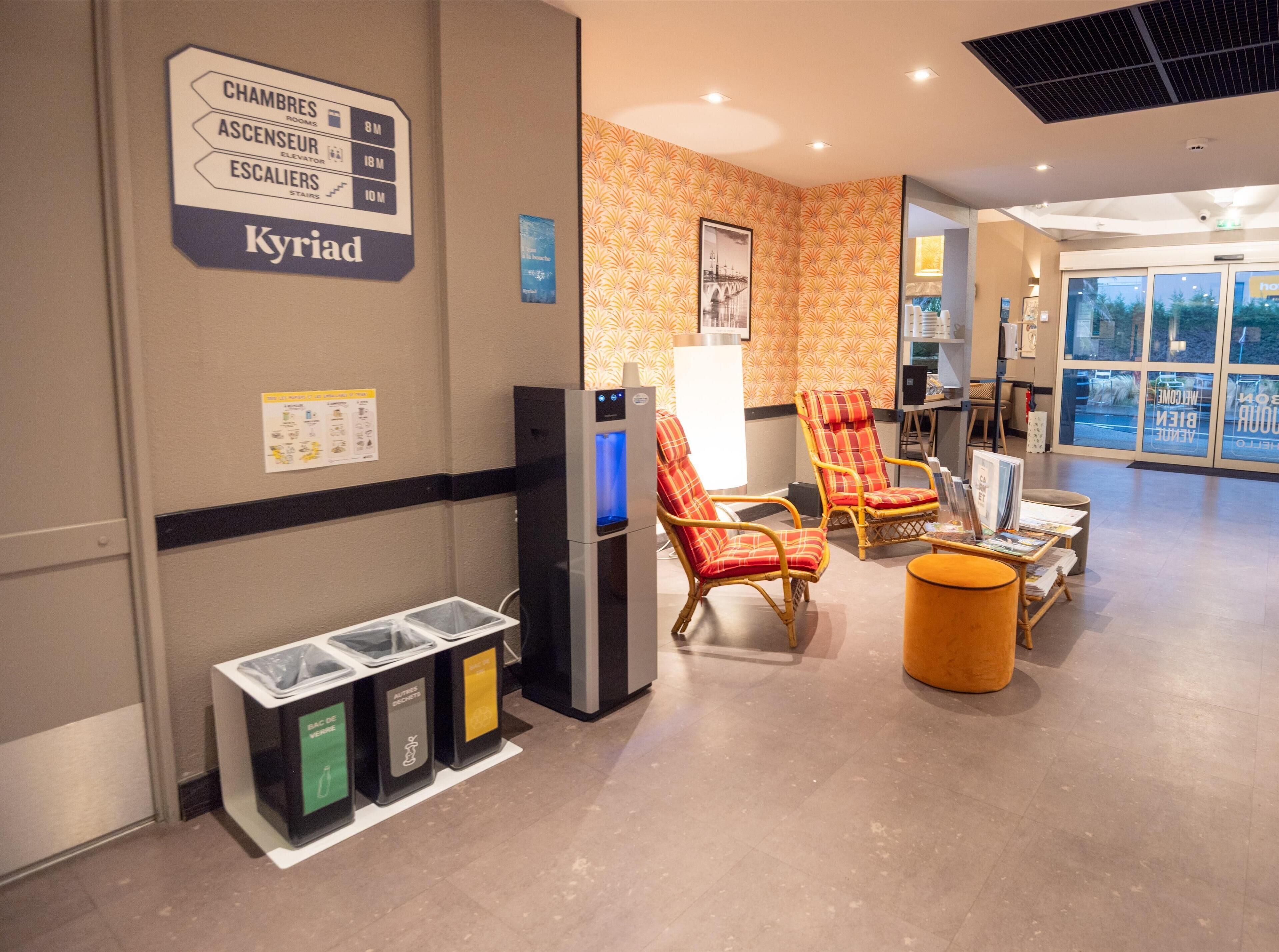 Un hall d’entrée équipé d’un distributeur d’eau, de poubelles et d’un espace détente avec des sièges.