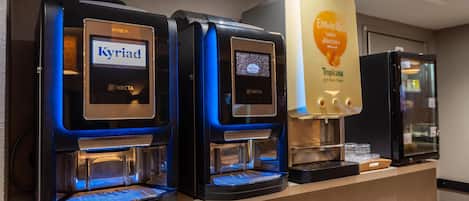 A row of coffee machines with brand labels, including KREA, Necta, and Tropicana, in a commercial setting.