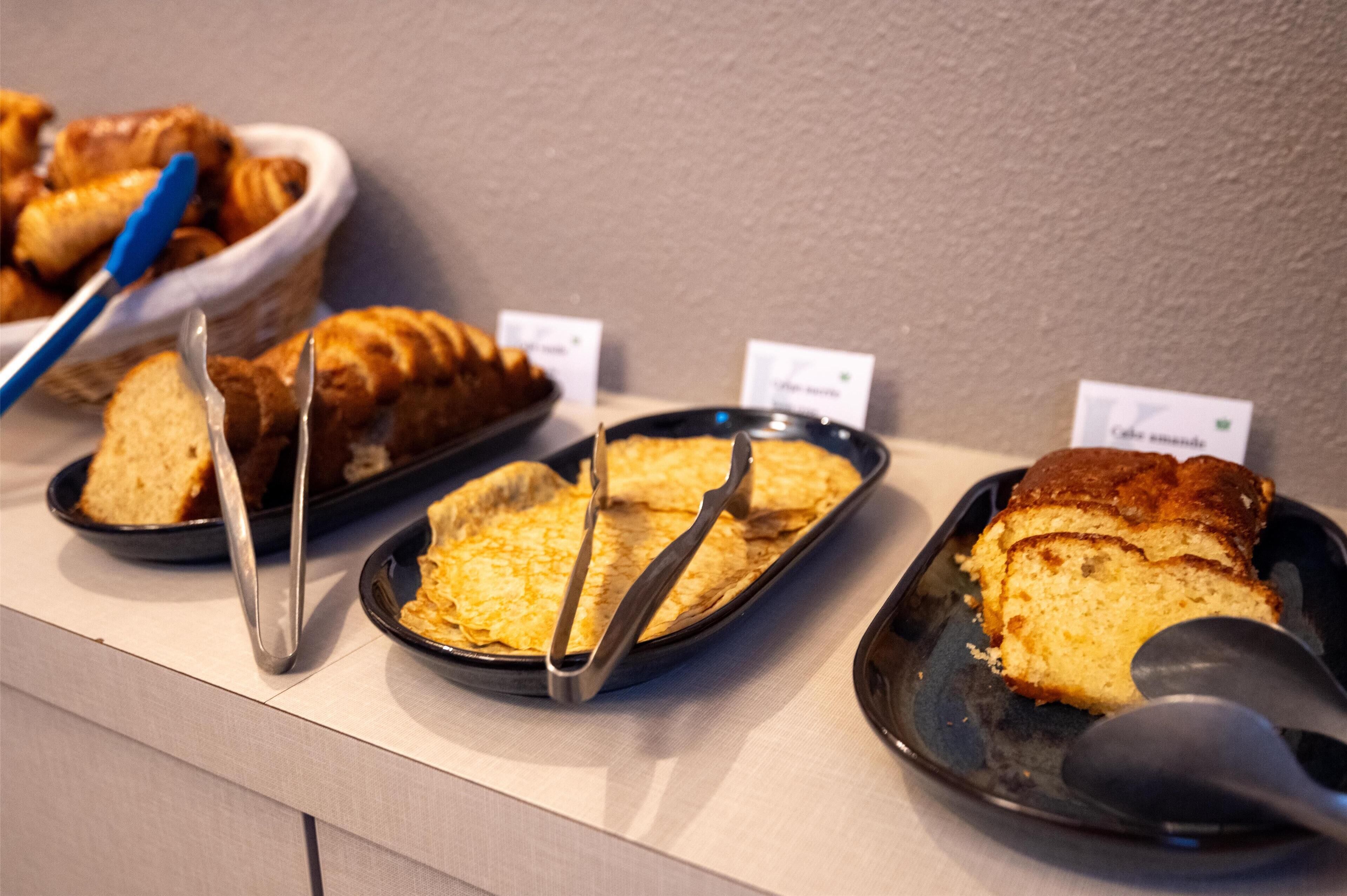 Eine Auswahl an Backwaren, darunter Brot und Gebäck, präsentiert auf einer Theke mit Preisschildern.